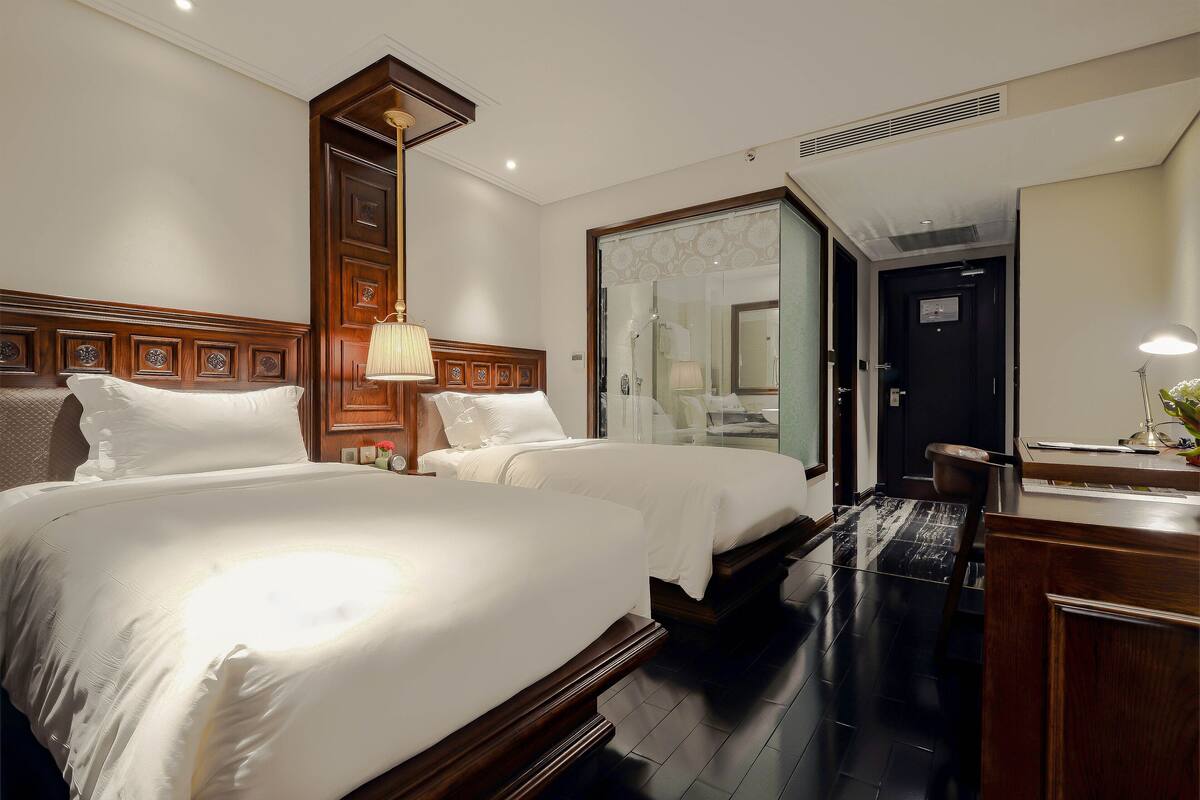 A hotel room with two beds, a wooden headboard, a desk, and a mirror.