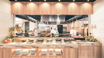 A modern kitchen with chefs preparing food, a wooden counter with dishes, and a brick wall.