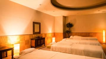 A hotel room with two beds, a small table, a mirror, and a plant.