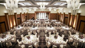 Un amplio salón de banquetes con mesas redondas, candelabros y un escenario al frente.