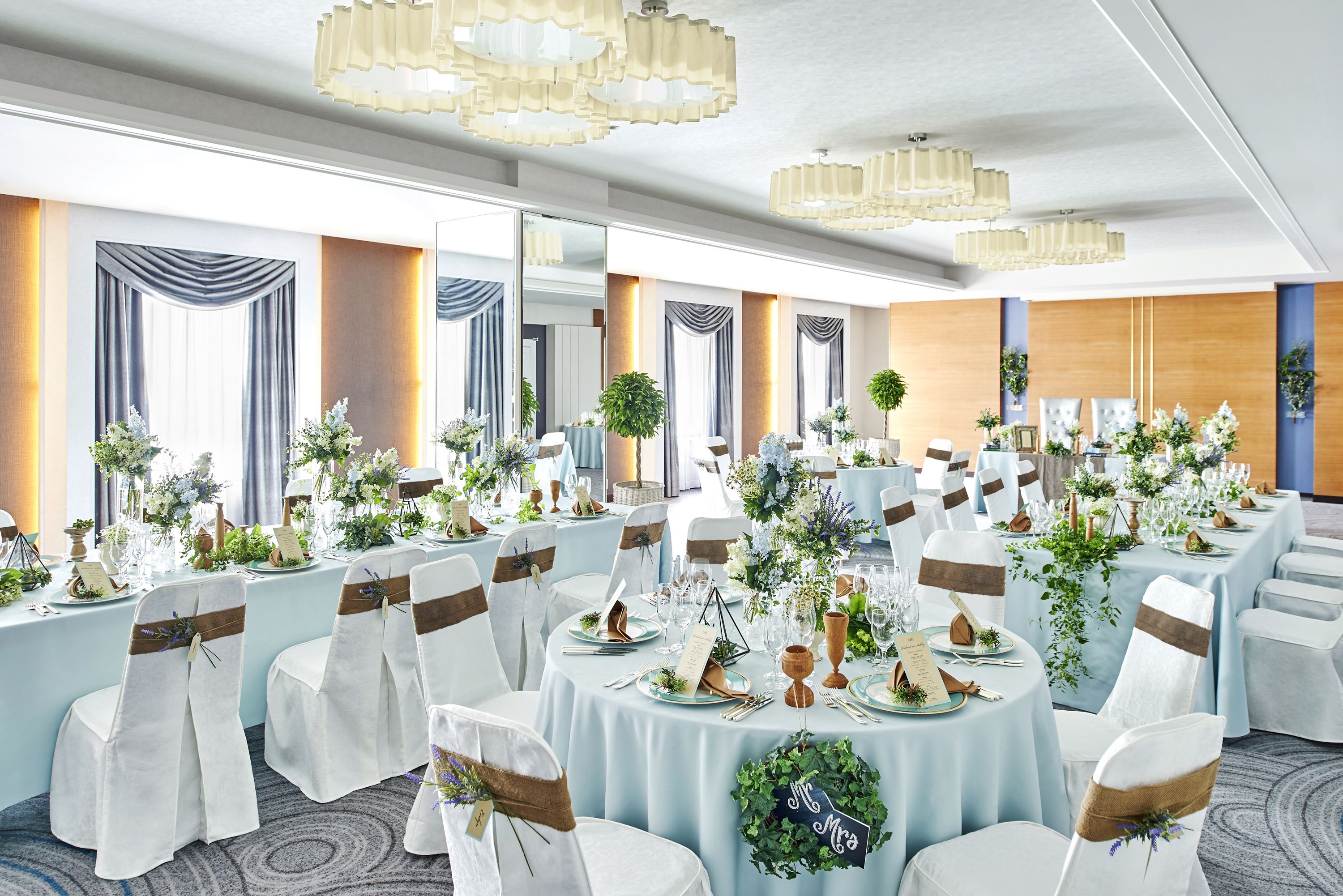 A banquet hall with round tables, white chairs, and floral centerpieces.