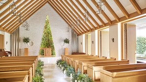 Interior de una iglesia con bancas de madera, un pasillo central y un gran árbol de Navidad.
