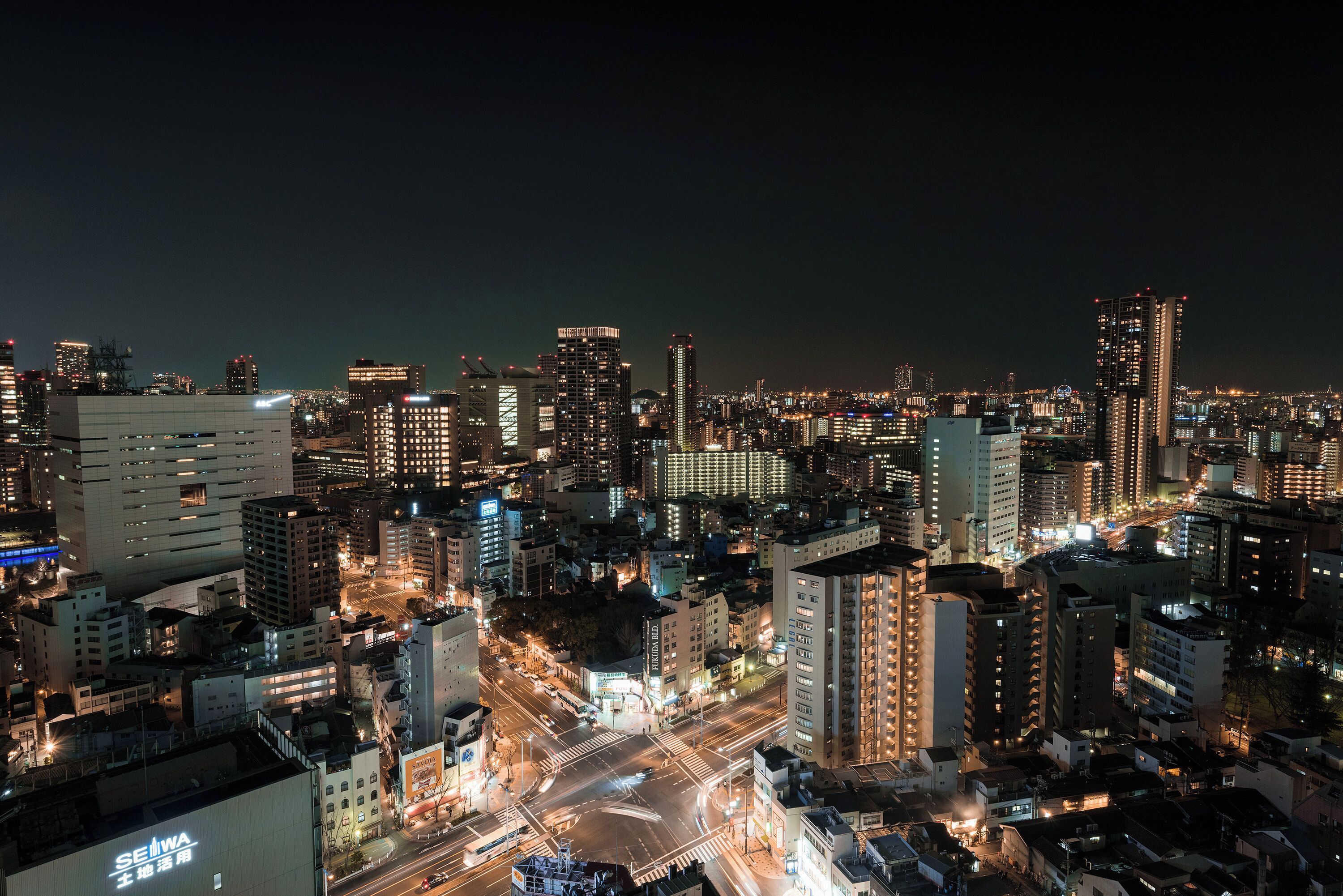 A nighttime cityscape with illuminated buildings and a busy intersection.