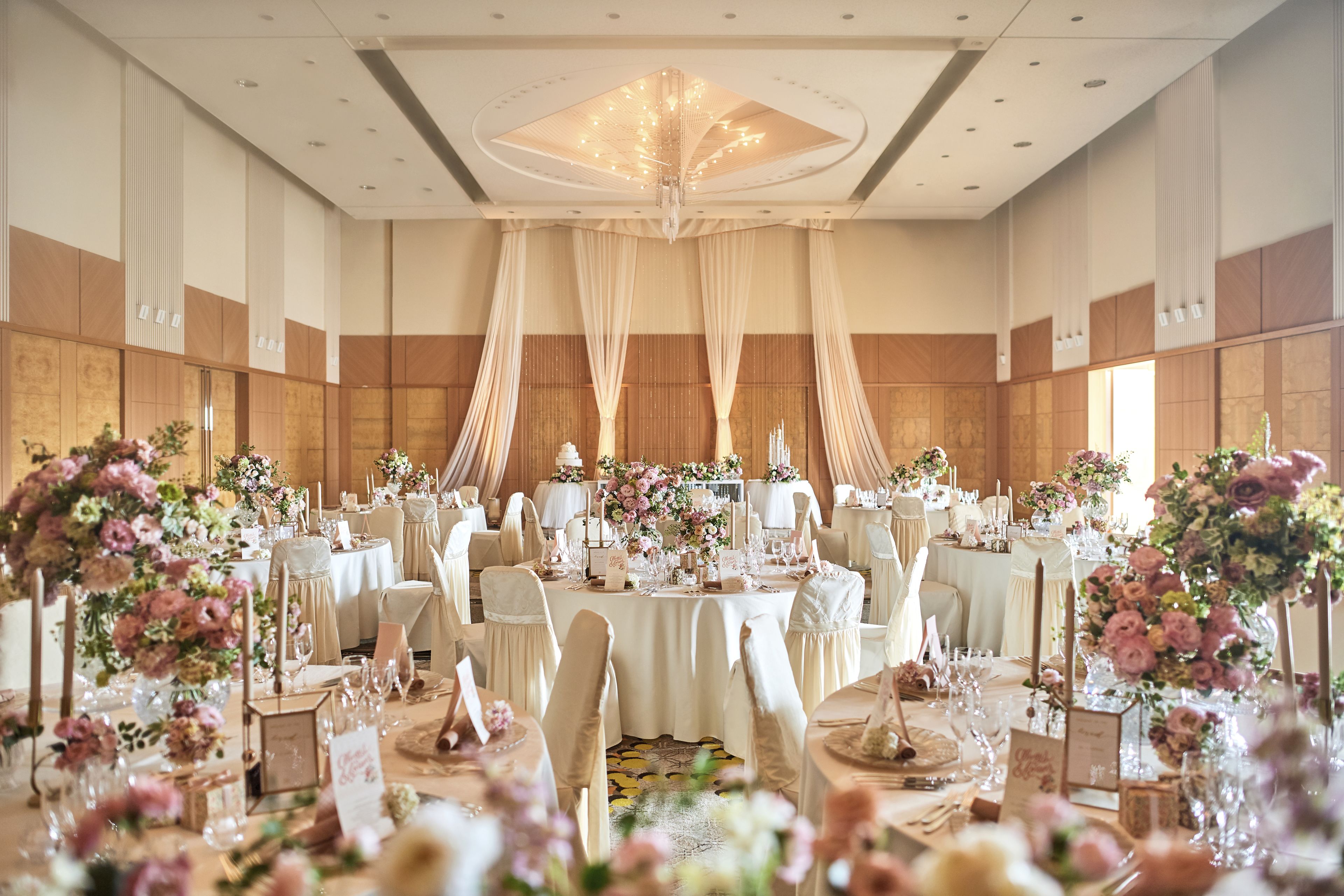 Une salle de banquet avec des tables rondes, des nappes blanches et des centres de table floraux.