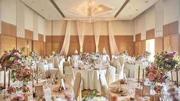 Une salle de banquet avec des tables rondes, des nappes blanches et des centres de table floraux.