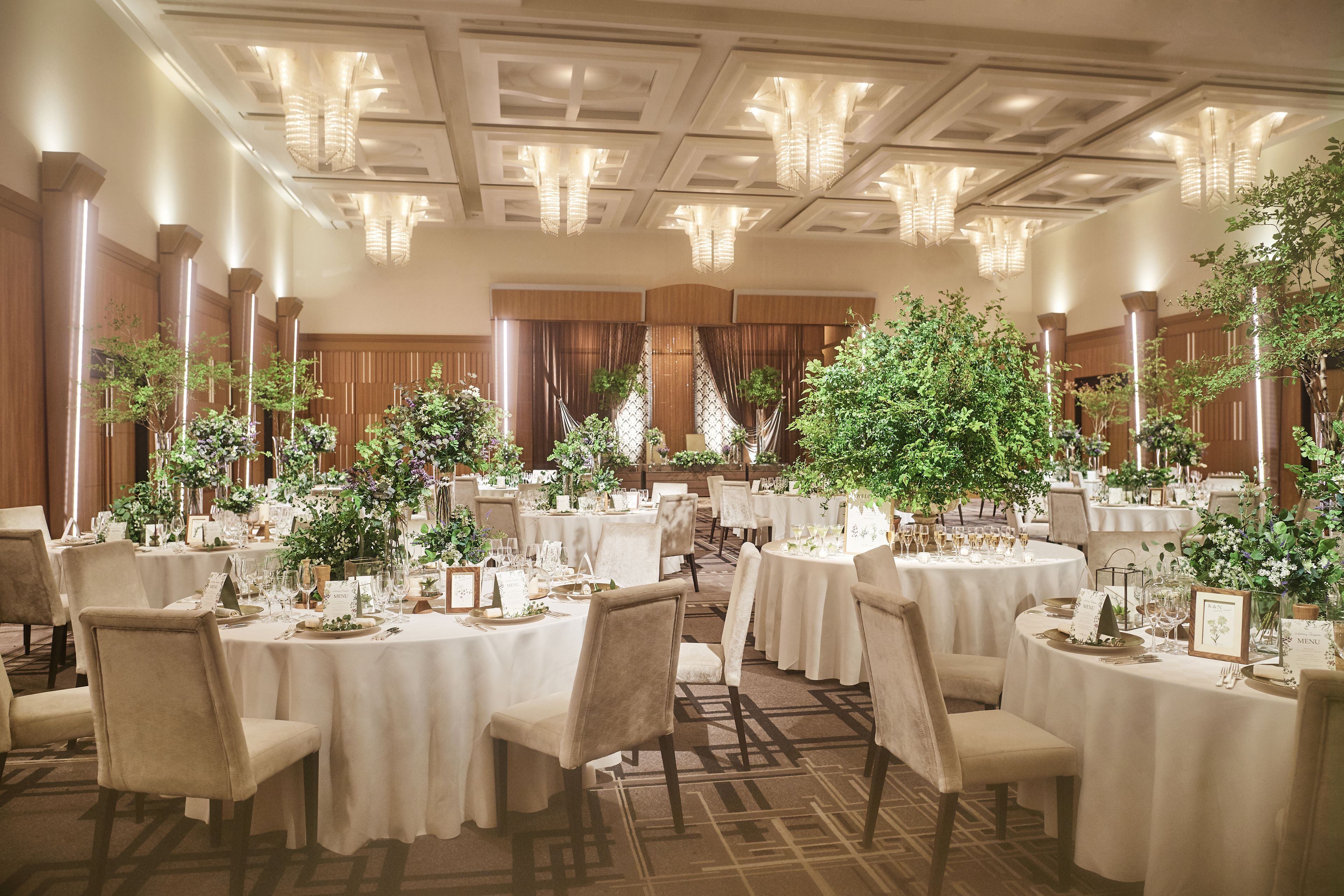 A banquet hall with round tables, chairs, and floral centerpieces.