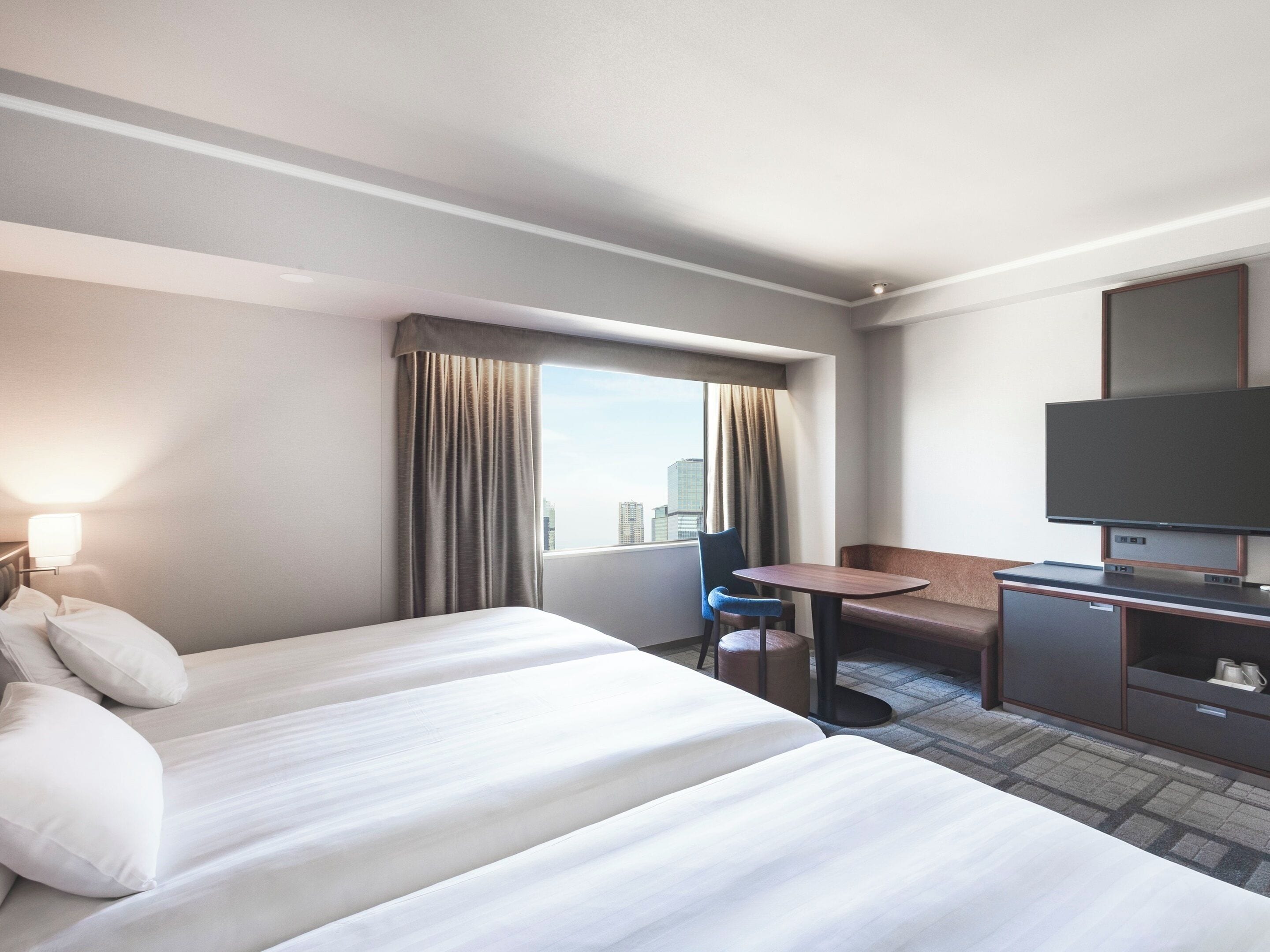 A hotel room with two beds, a desk, a chair, a television, and a window with curtains.