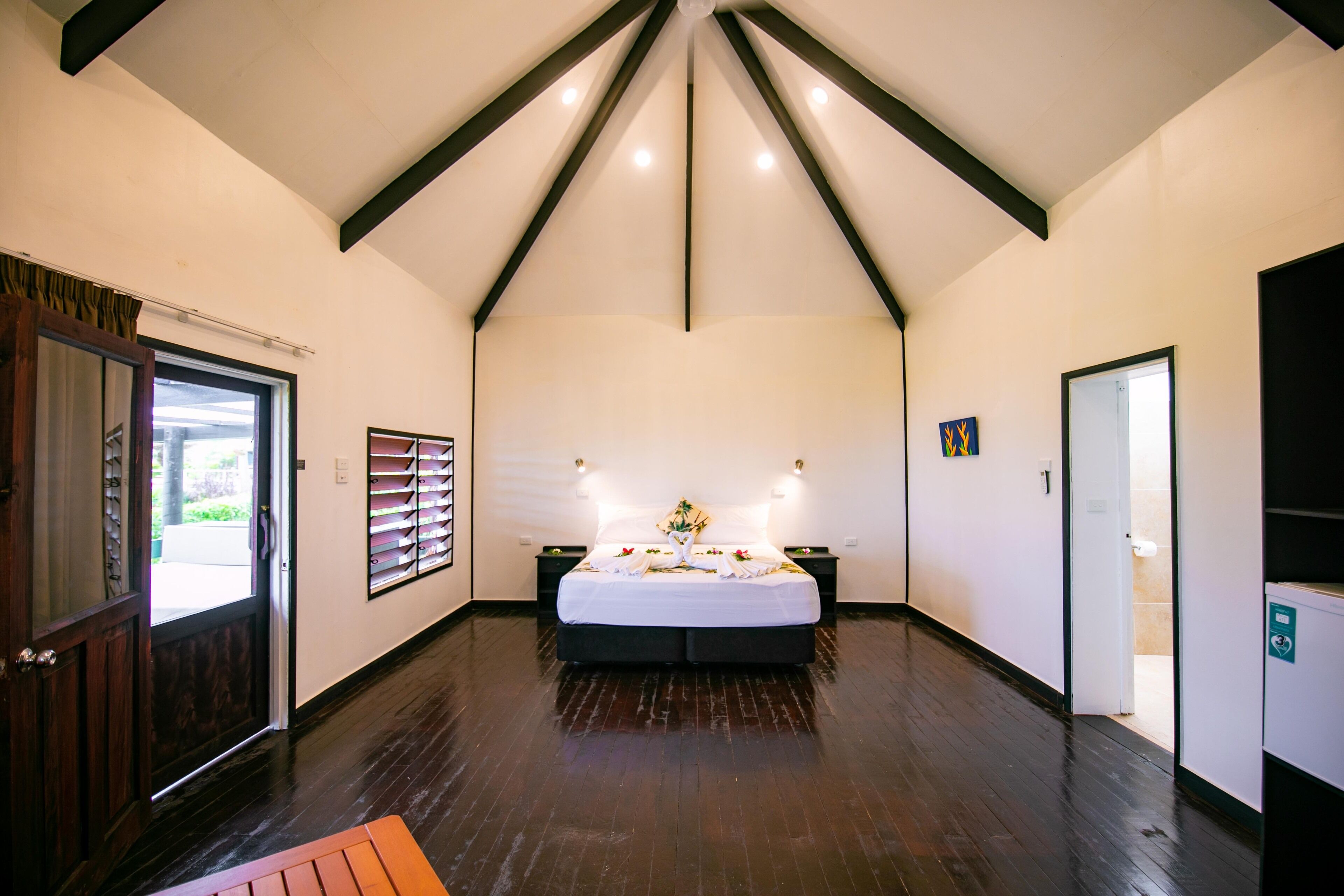 Una habitación amplia con una cama grande, suelo de madera y techo inclinado con vigas a la vista.