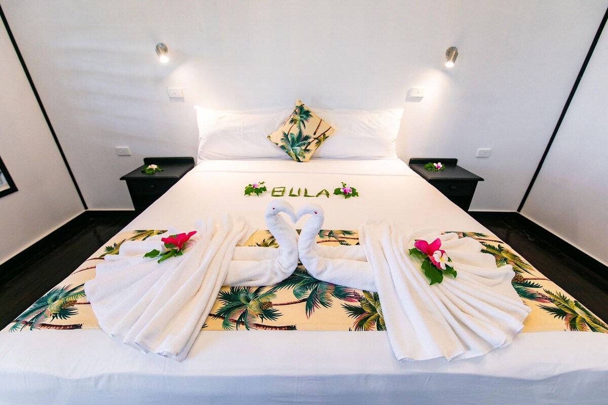 Una habitación de hotel con una cama, dos mesitas de noche y una lámpara de pared.