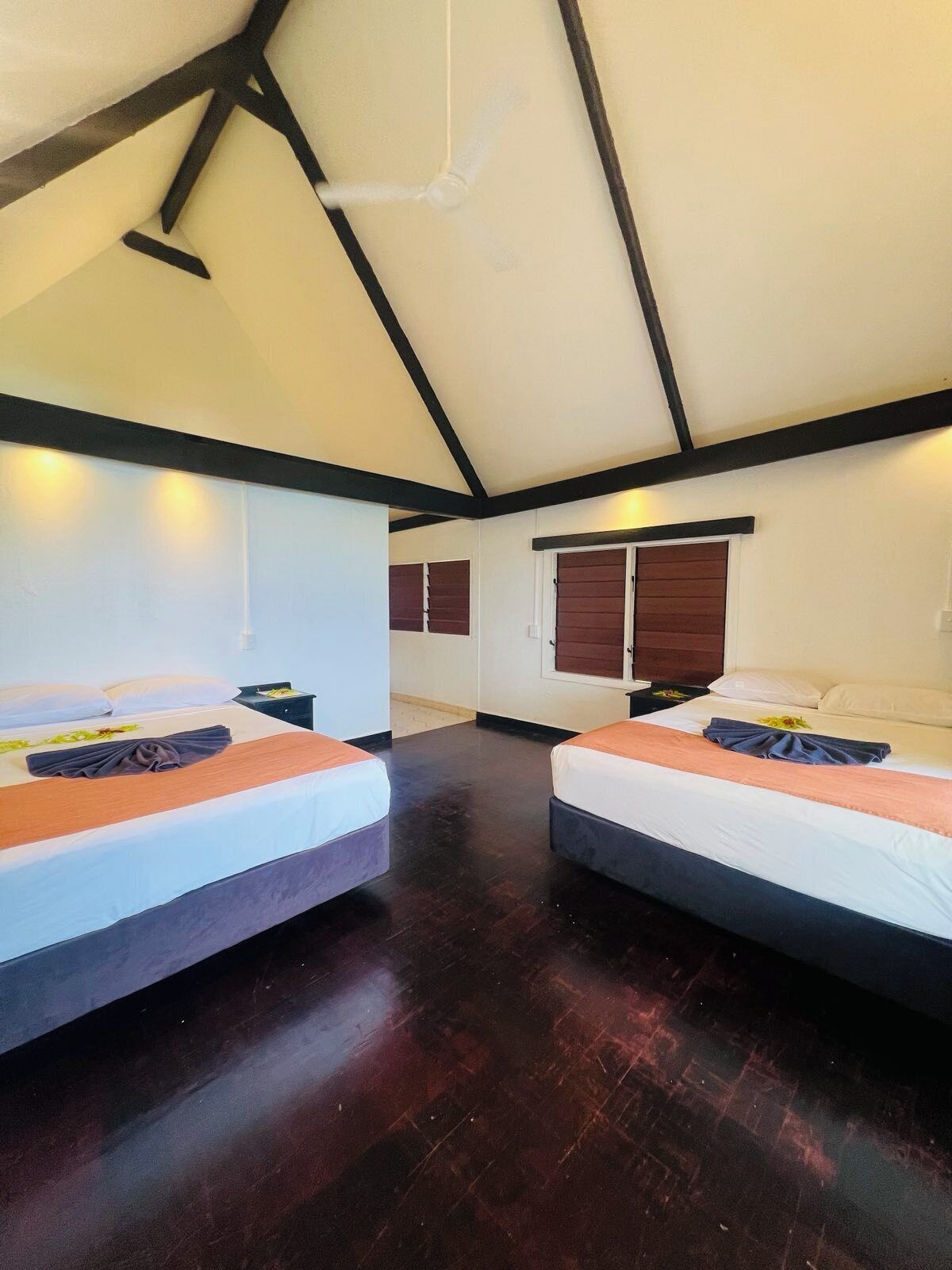 A room with two beds, wooden flooring, and a sloped ceiling with exposed beams.