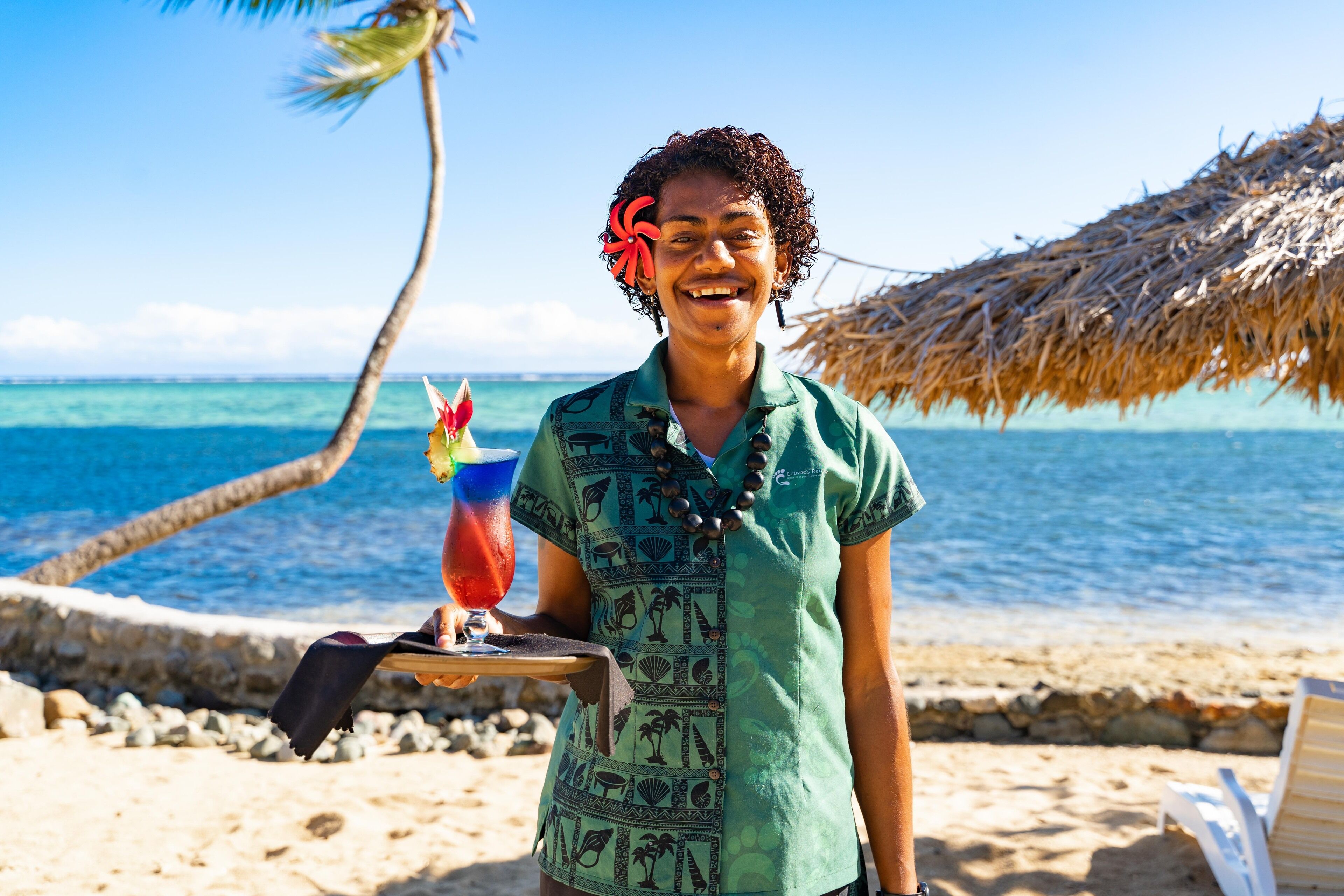 A person standing on a beach with a drink in hand, palm trees, and a clear blue sky.