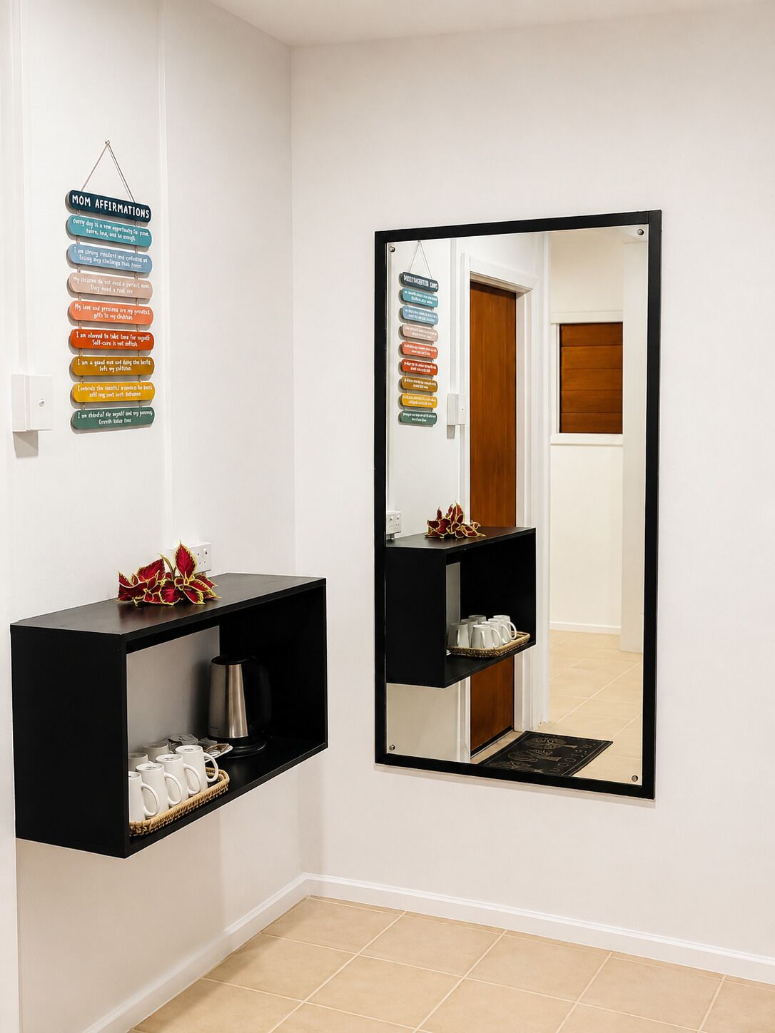 A hallway with a black shelf unit containing a coffee maker and cups, a mirror reflecting a door and a window, and a wall with a 'Mom Affirmations' sign.