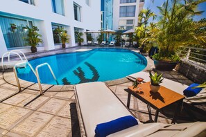 A pool area with lounge chairs, a small table, and potted plants. - Mondial Hotel Hue (Hue)