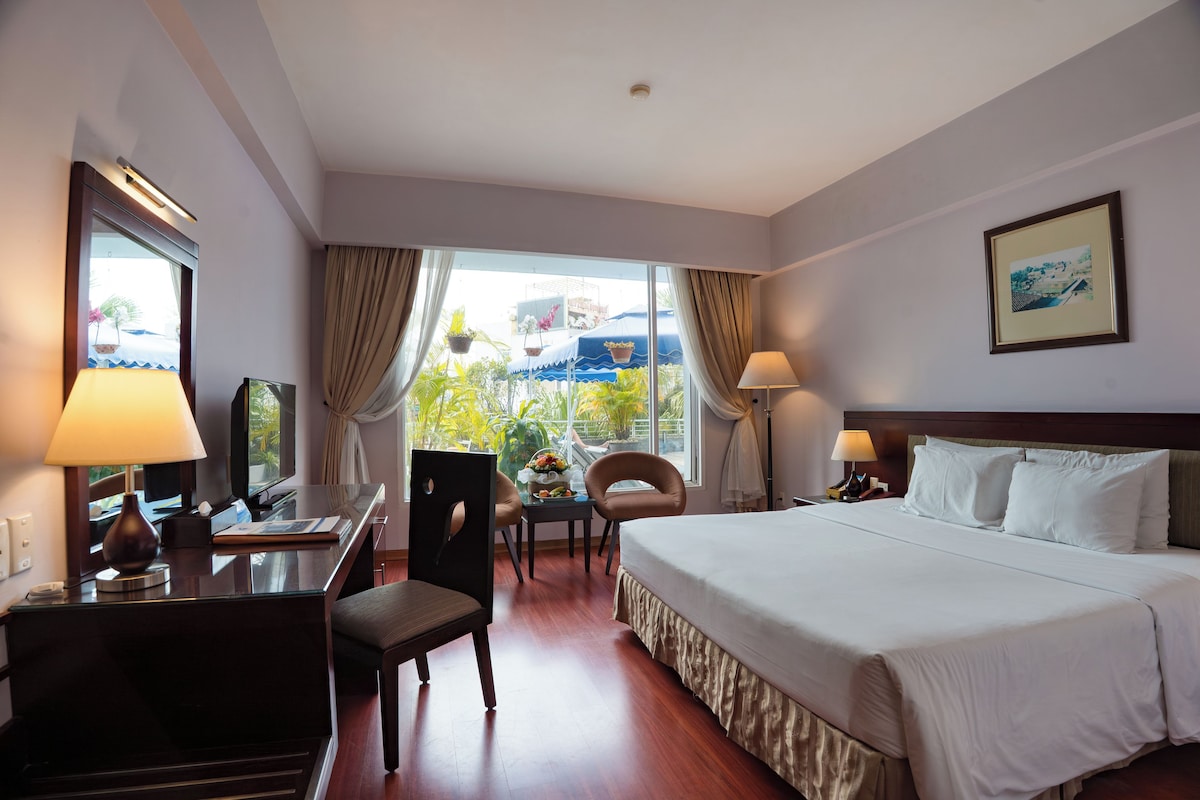 A hotel room with a bed, desk, chairs, and a window with curtains.