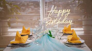 A table set for a birthday celebration with a neon sign, a view of a cityscape, and a blue tablecloth.