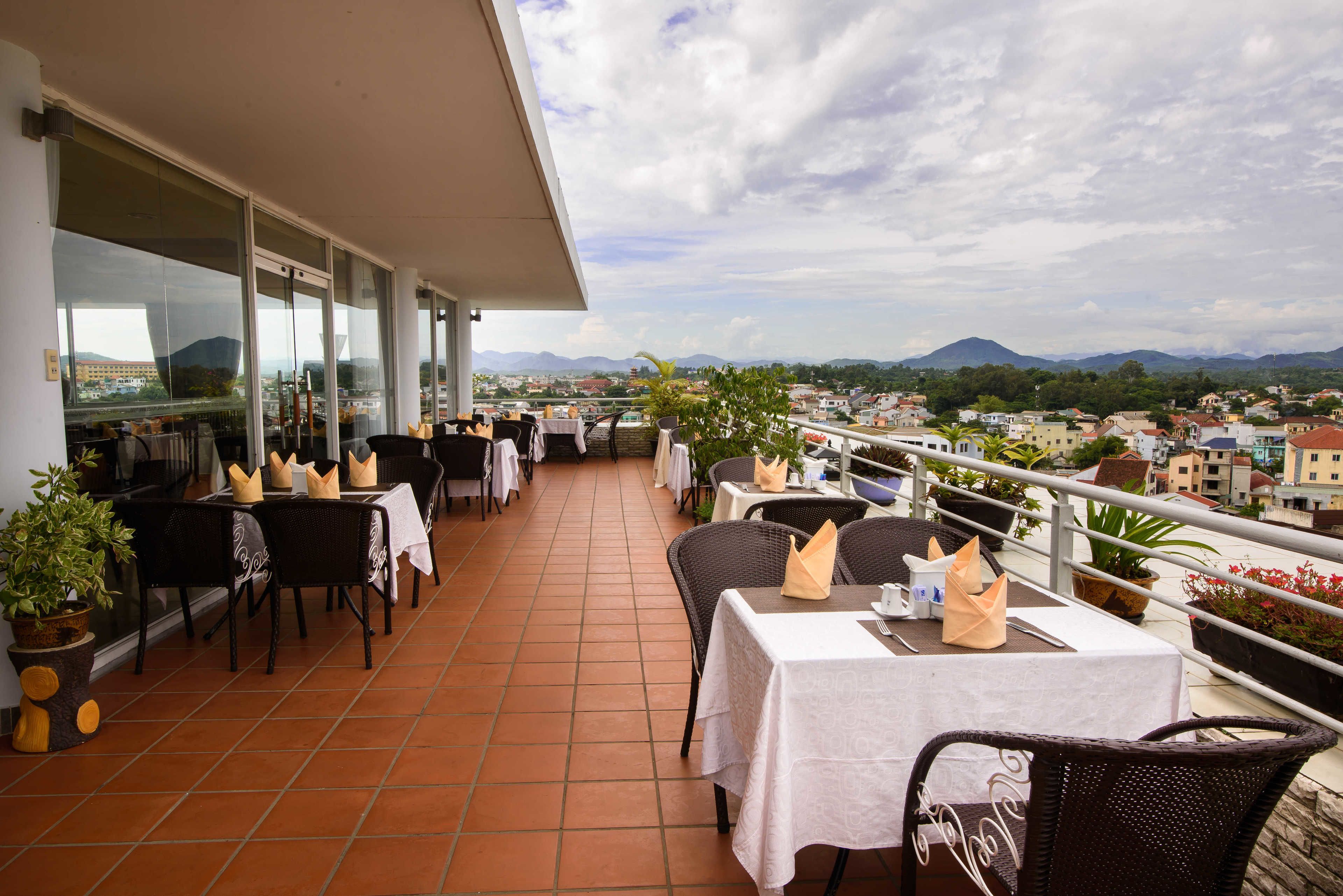 Una terraza con mesas y sillas, una barandilla y vistas a la ciudad y las montañas.