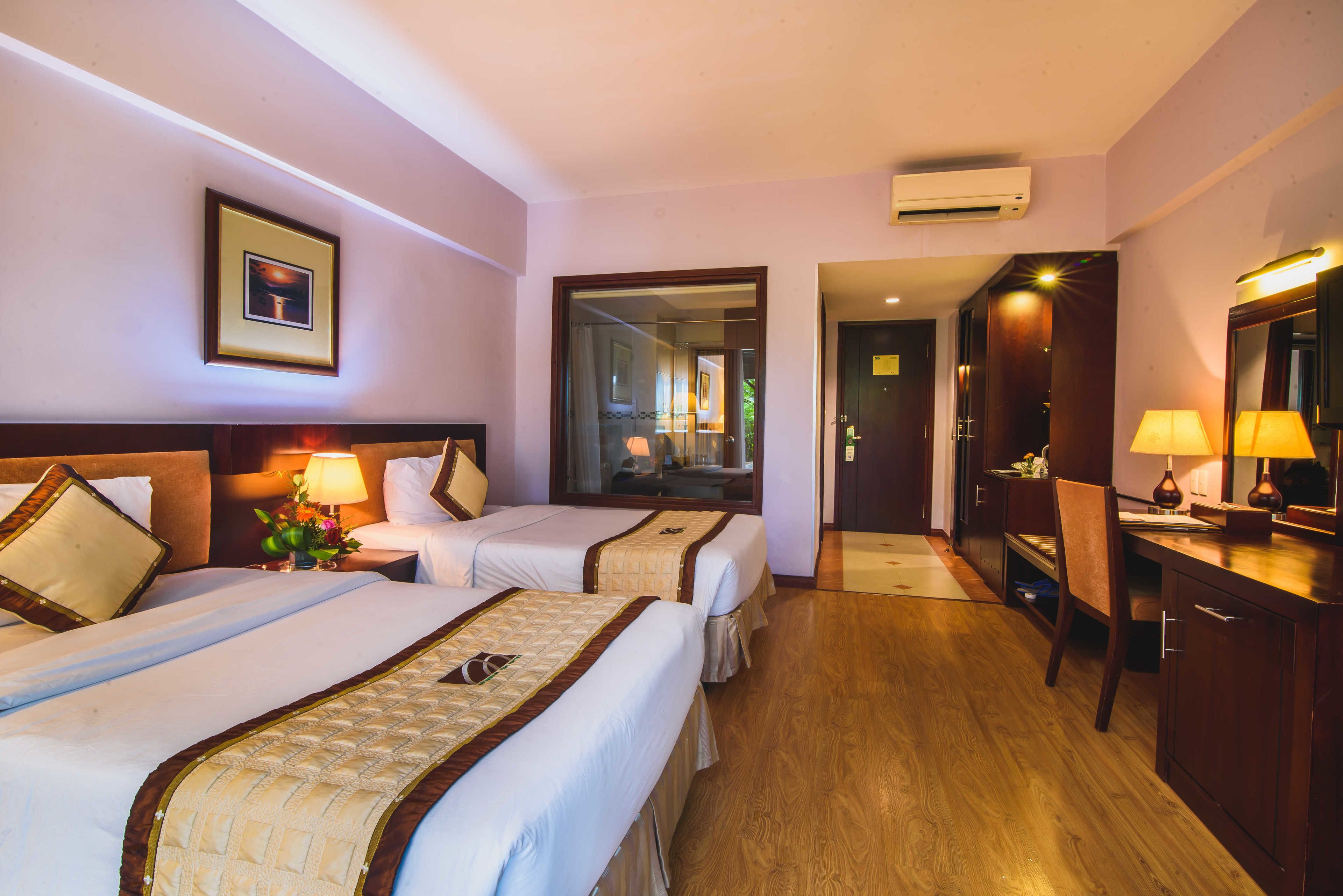 A hotel room with two beds, a desk, a chair, a mirror, and an air conditioning unit.