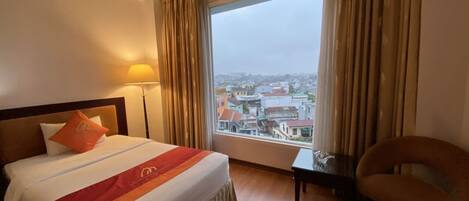 A hotel room with a large bed, a view of the city, and a chair by the window.