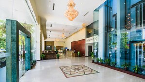 A spacious lobby with a reception desk, modern chandeliers, and potted plants.