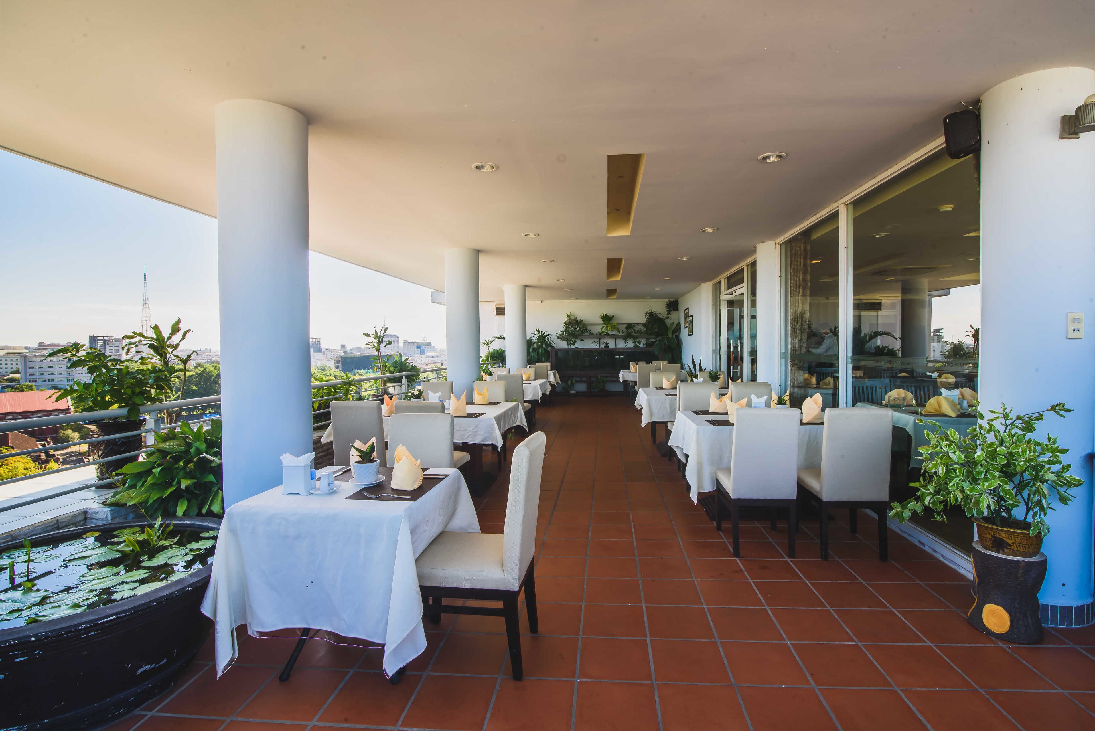 An outdoor dining area with tables and chairs, a water feature, and a view of the city skyline.
