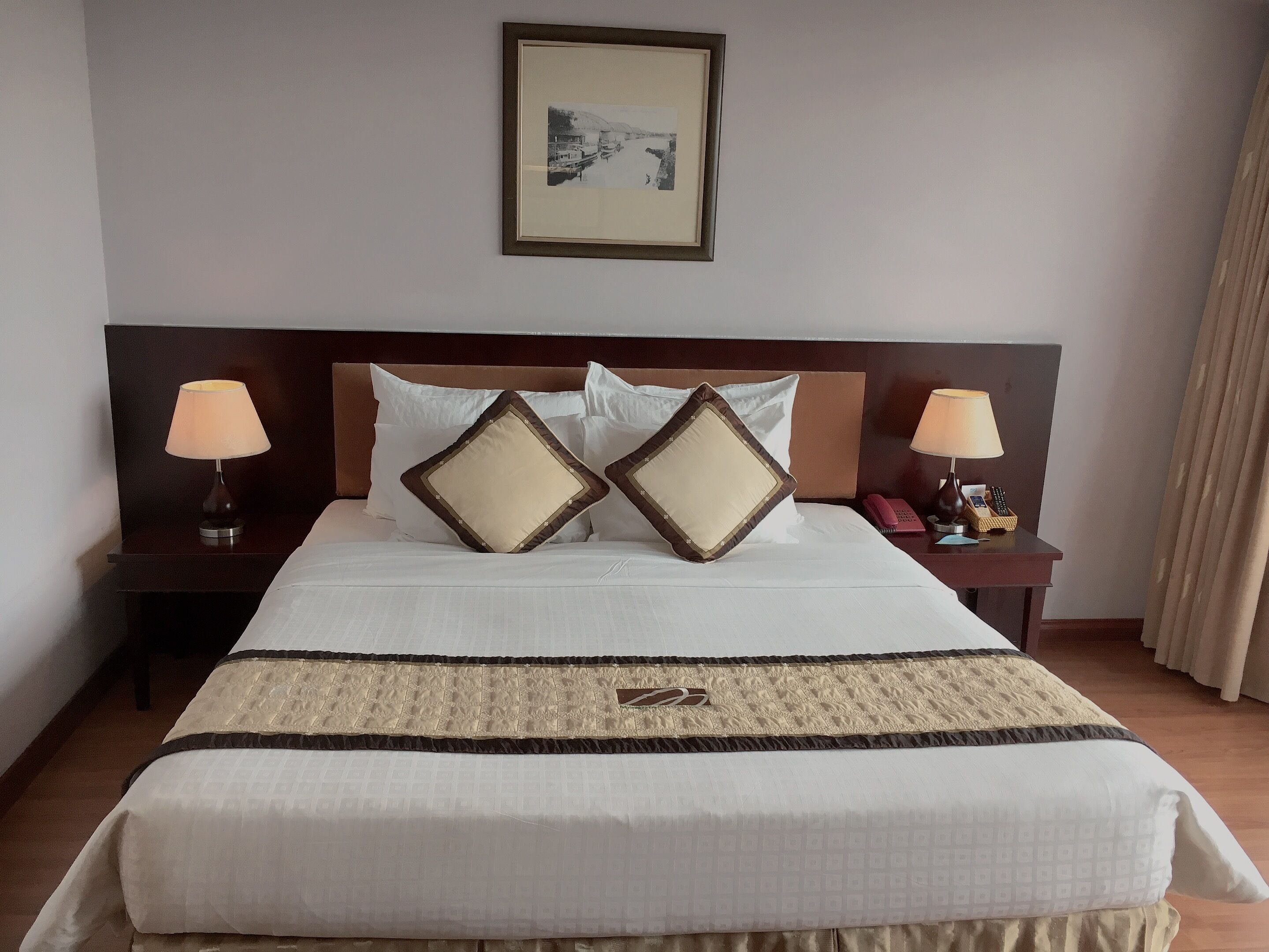 A neatly made bed with a patterned bedspread, two bedside lamps, a framed picture on the wall, and a bedside telephone.
