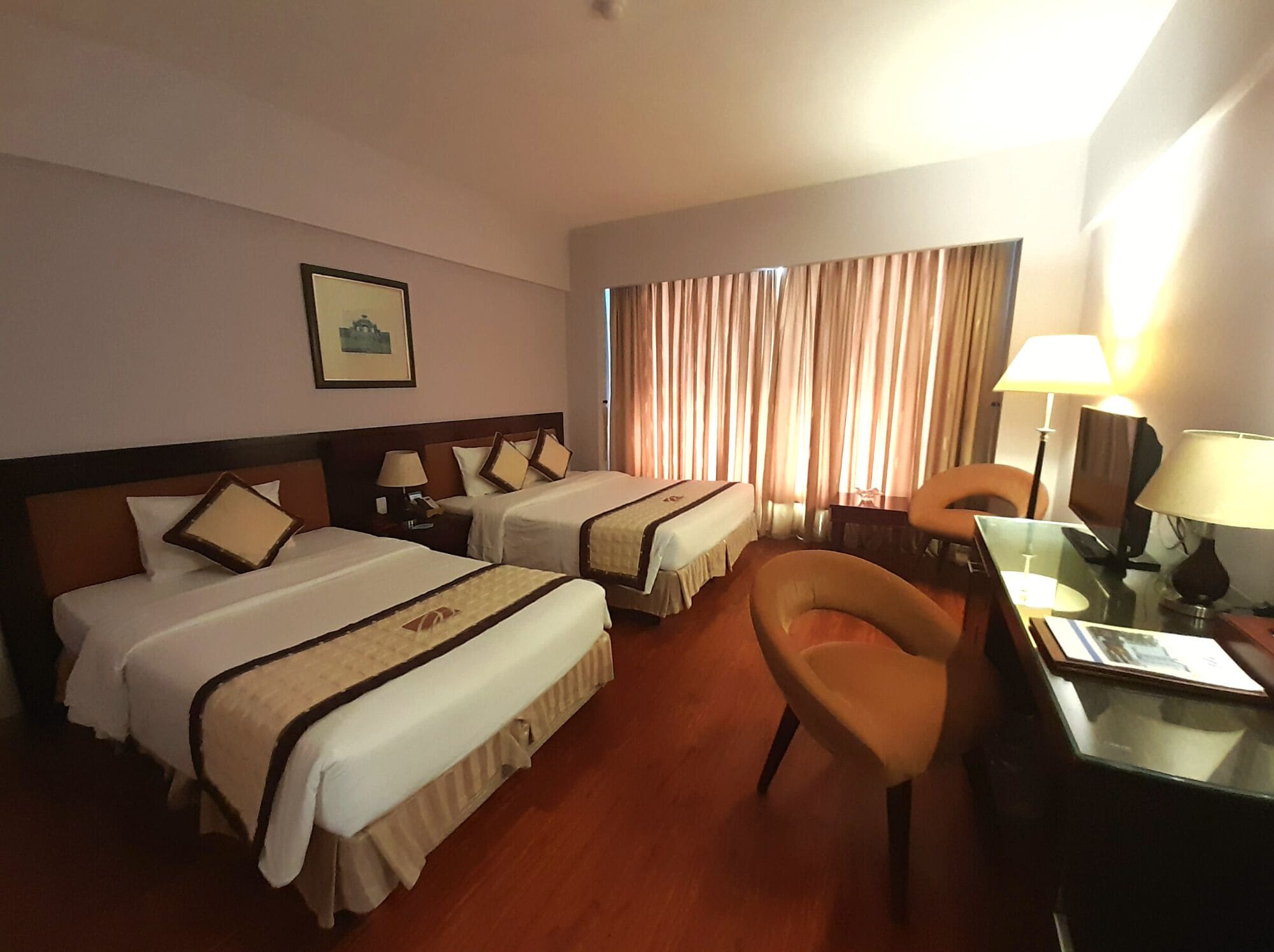 A hotel room with two beds, a desk, a chair, and a lamp.
