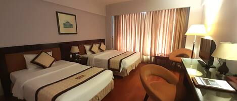A hotel room with two beds, a desk, a chair, and a lamp.