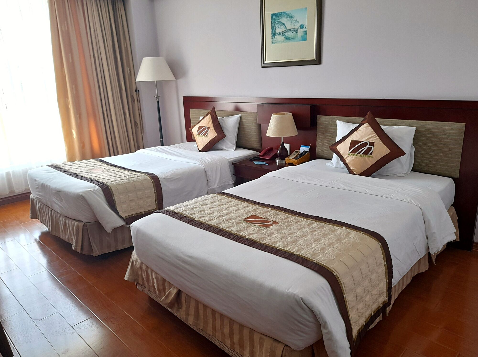 A hotel room with two beds, each with a headboard, bedside tables, lamps, and decorative pillows.