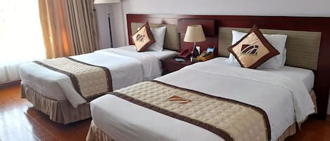 A hotel room with two beds, each with a headboard, bedside tables, lamps, and decorative pillows.