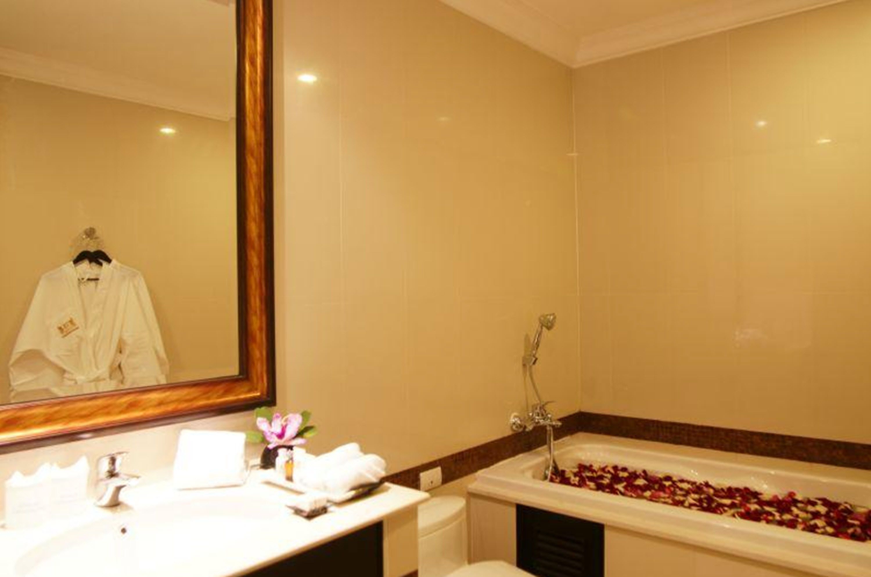A bathroom with a large mirror, a bathtub filled with rose petals, a white sink, and a towel rack.