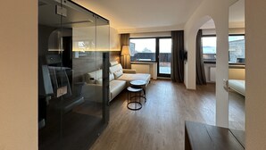Et moderne hotelværelse med glasvæg, en sofa, et lille rundt bord og udsigt til det fri.