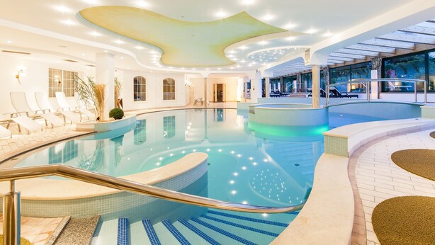 En moderne swimmingpool indendørs med krystalklart vand, liggestole og et glastag.