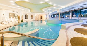 A modern indoor swimming pool with clear water, sun loungers, and a glass ceiling. - Royal Hotel Hinterhuber (Brunico)