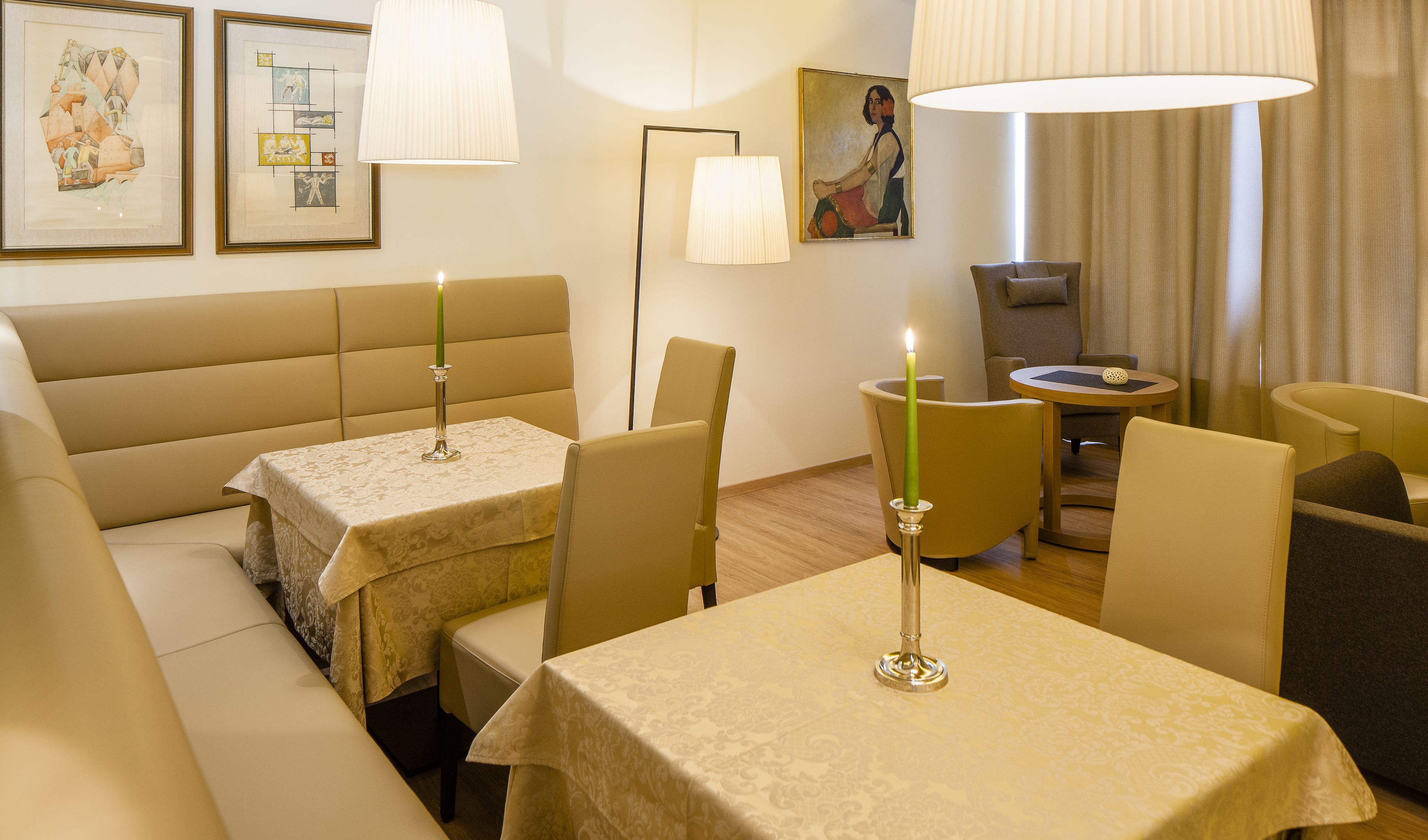 Una habitación de hotel con un sofá, dos mesitas con velas, una lámpara y obras de arte en las paredes.
