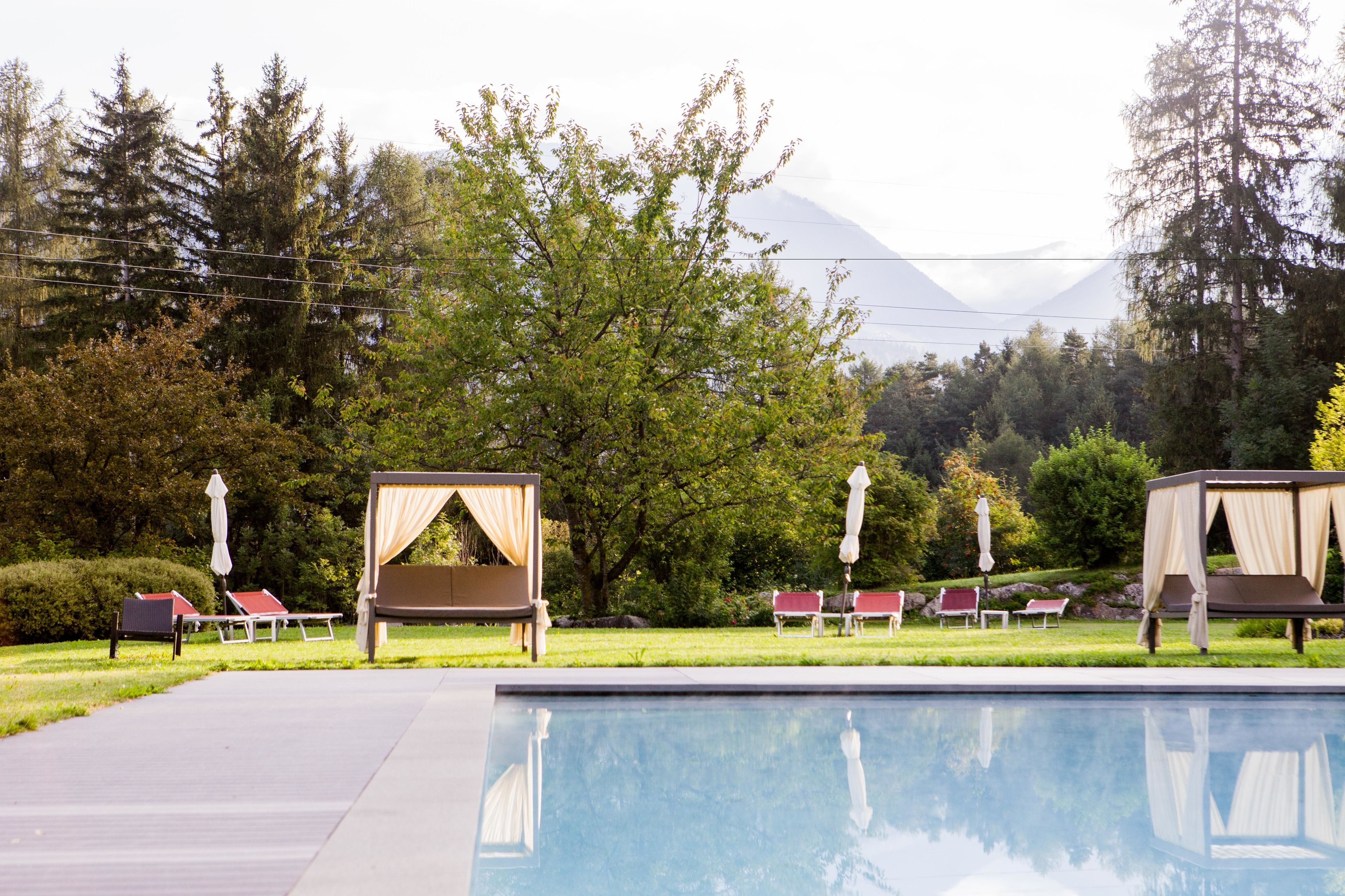 A pool area with lounge chairs and a canopy bed, surrounded by trees and a mountain in the background.