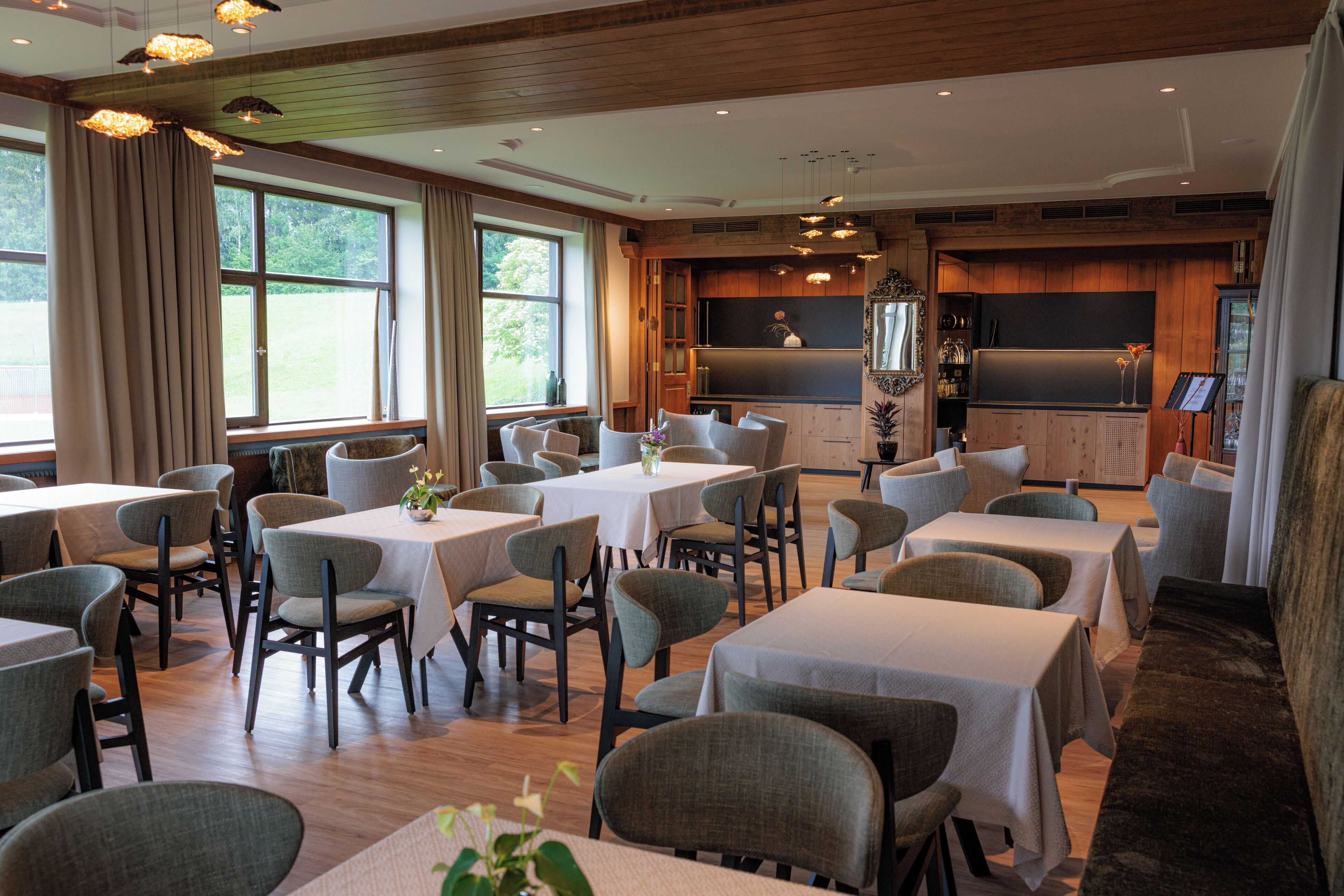 A dining area with multiple tables and chairs, large windows, and a wooden ceiling.