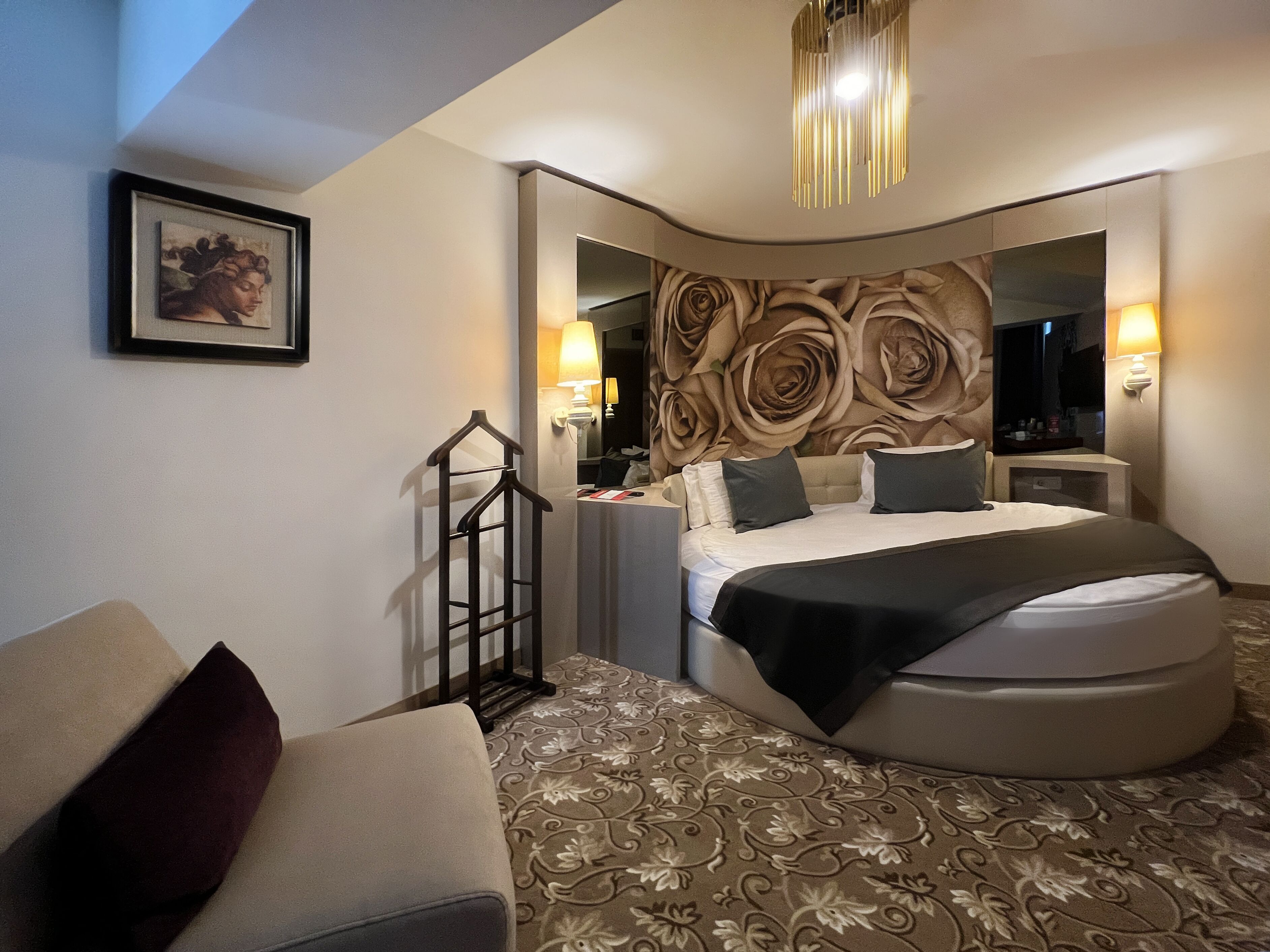 A modern hotel room with a curved bed, a large mirror, and a decorative wall.