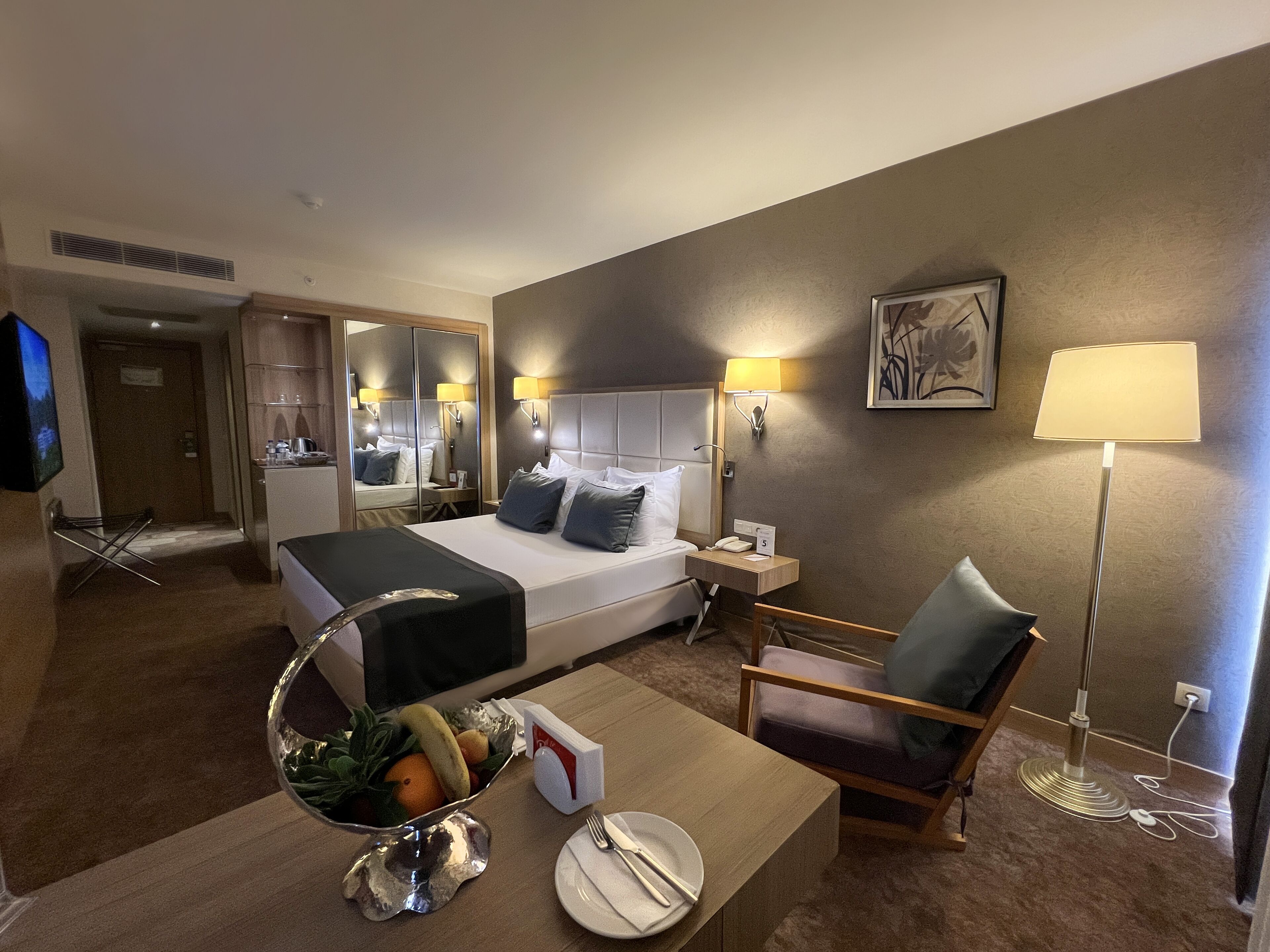 Quarto de hotel com cama, mesa de cabeceira, cadeira e espelho.