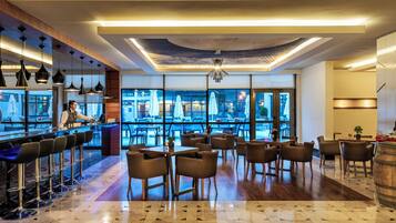 A modern bar area with a bartender, a seating area with tables and chairs, and large windows offering a view of the outdoor seating area.