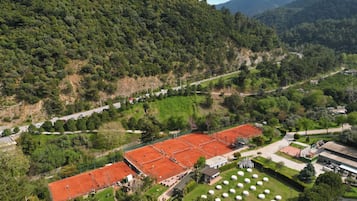 An aerial view of a tennis court surrounded by lush greenery and a mountainous backdrop.