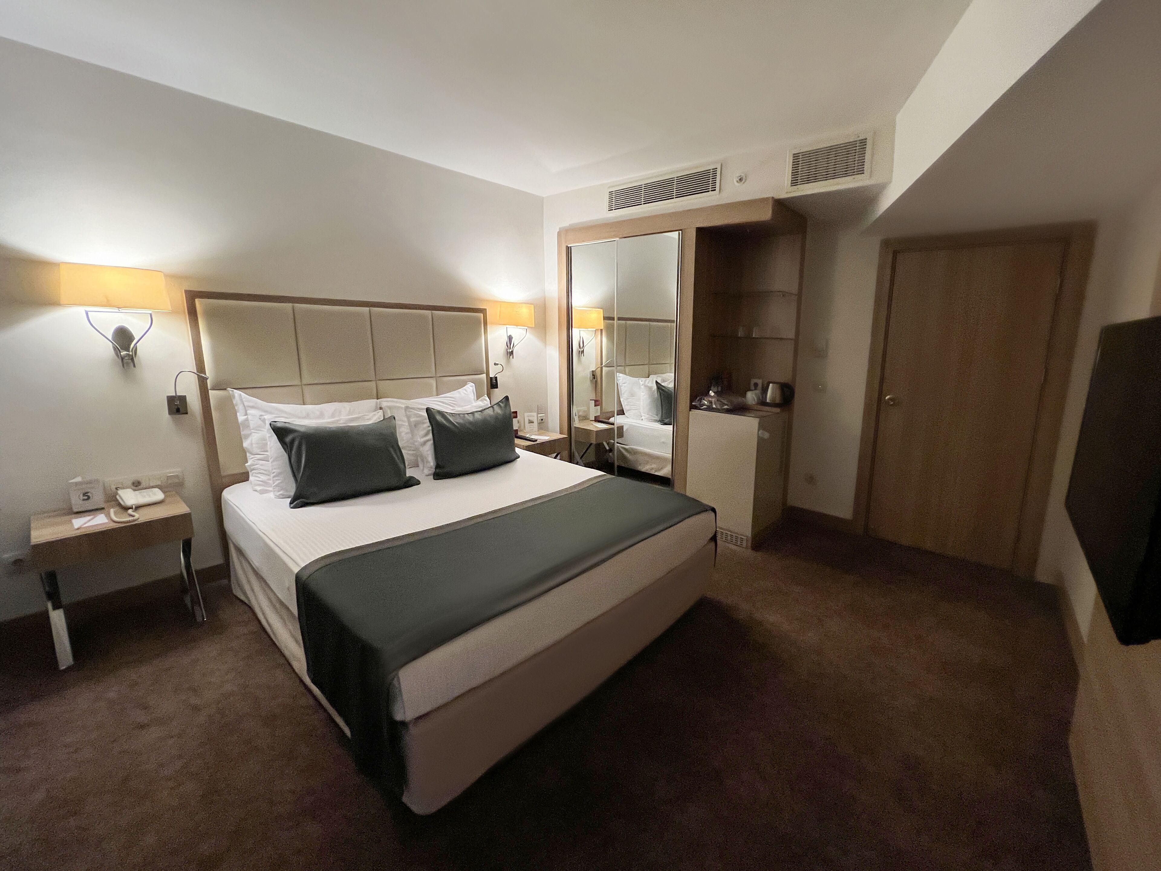 A hotel room with a bed, bedside table, lamp, mirror, and wardrobe.