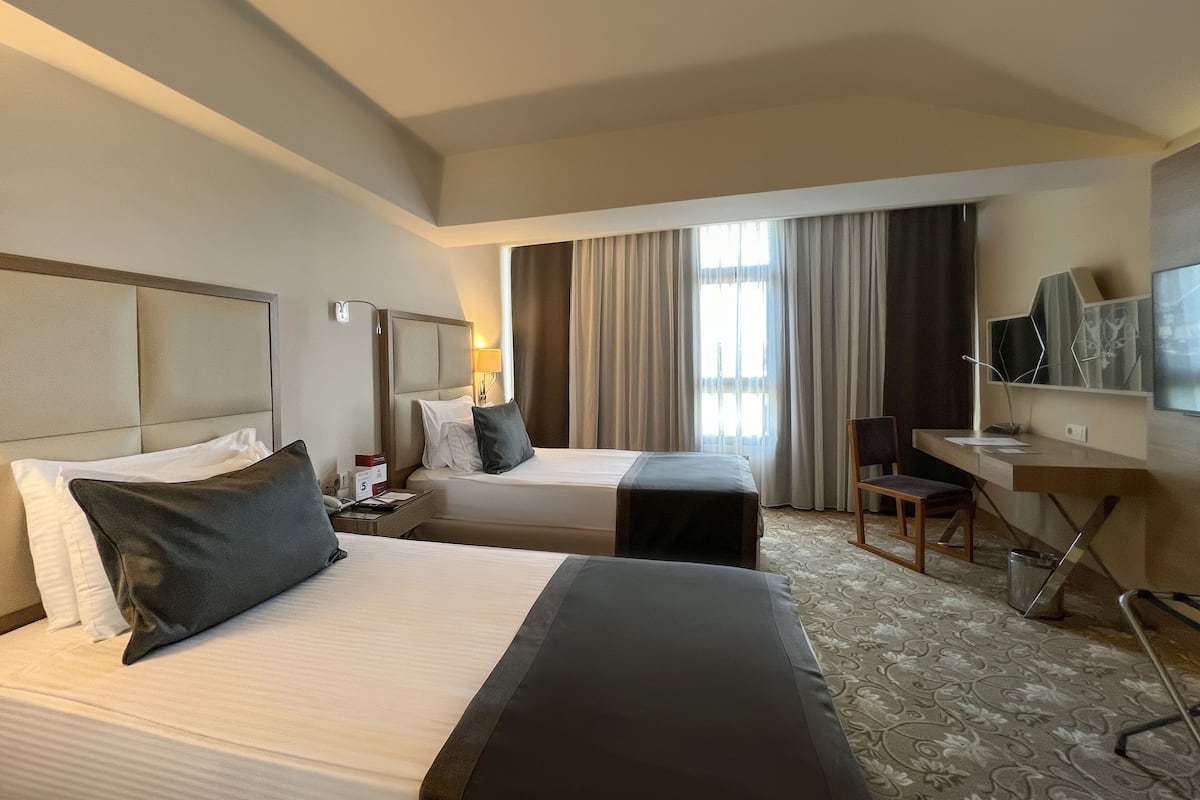 A hotel room with two beds, a desk, a chair, and a television.