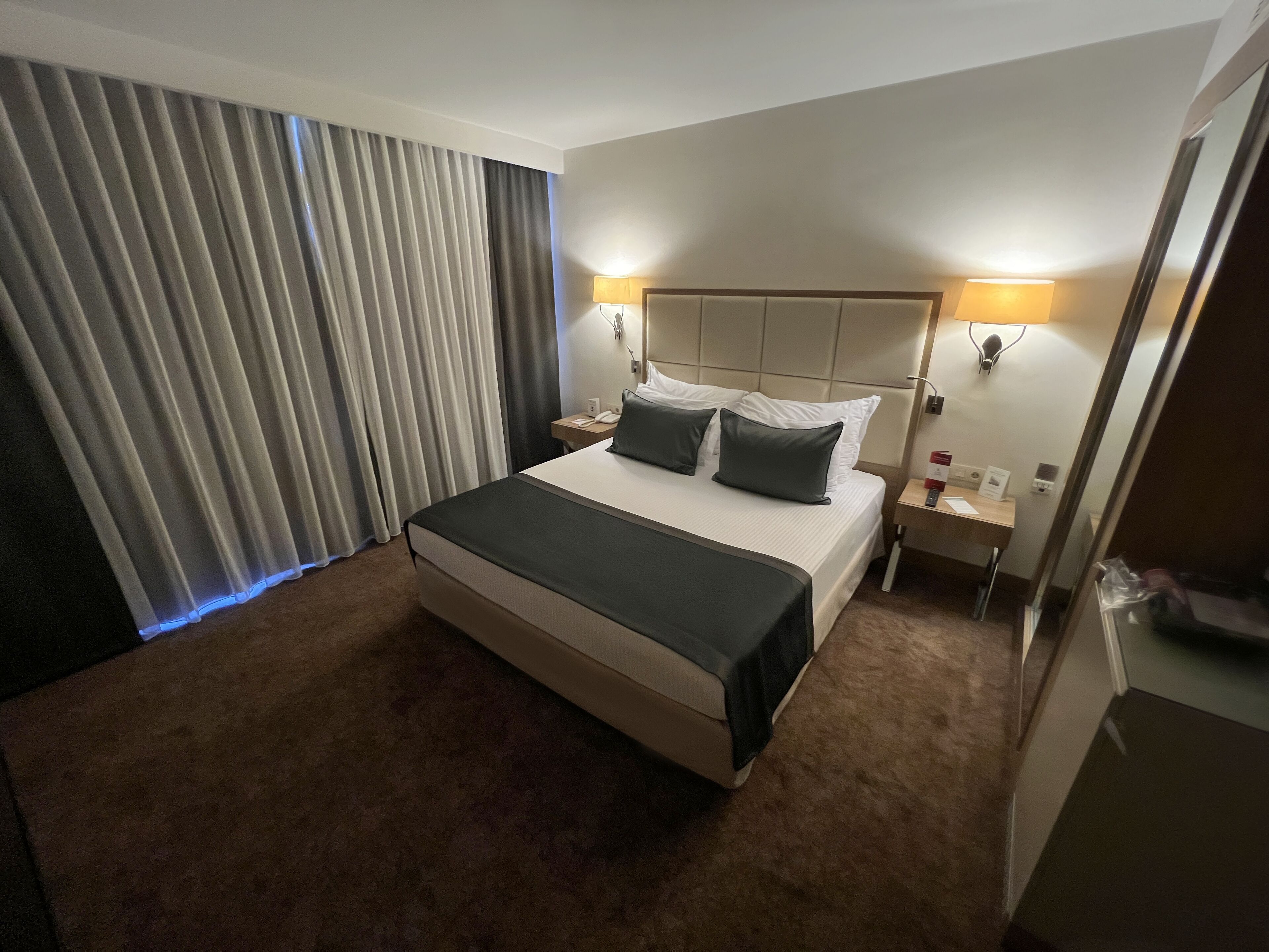 Une chambre d’hôtel avec un grand lit, deux lampes de chevet, une table de chevet, un bureau et une fenêtre avec des rideaux.