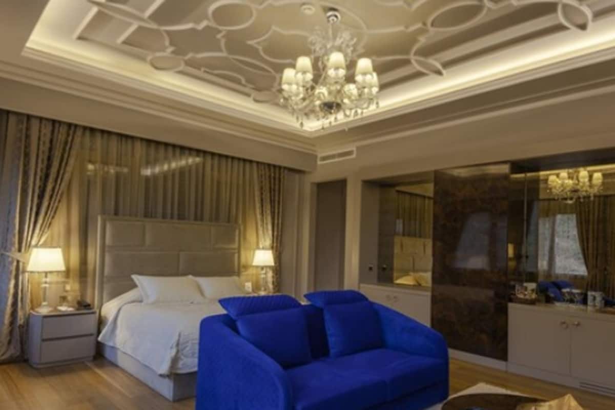 A bedroom with a large bed, a blue sofa, a chandelier, and a mirror.