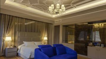 A bedroom with a large bed, a blue sofa, a chandelier, and a mirror.