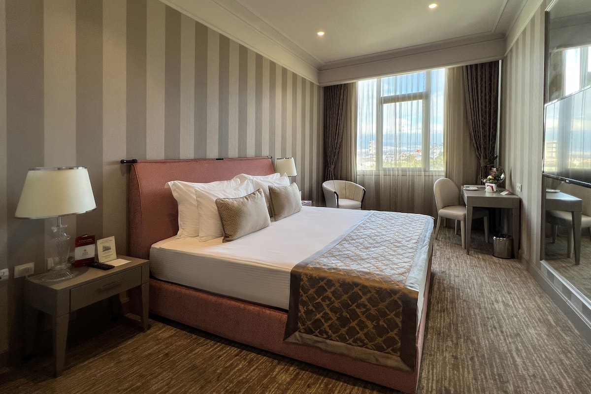 A hotel room with a large bed, a desk, a chair, and a TV.