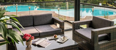 Un balcon donnant sur une piscine, avec des meubles en osier et un vase de fleurs.