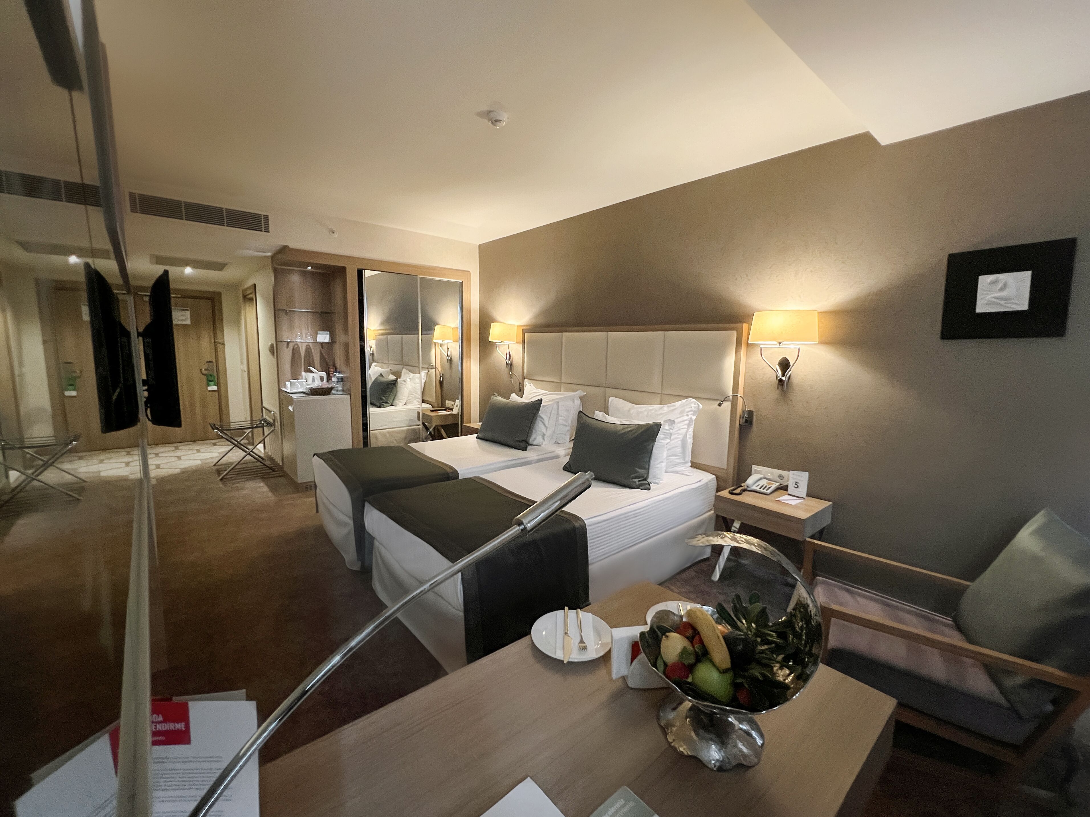 Une chambre d’hôtel avec un lit, une table de chevet et une petite table à manger agrémentée d’un panier de fruits.