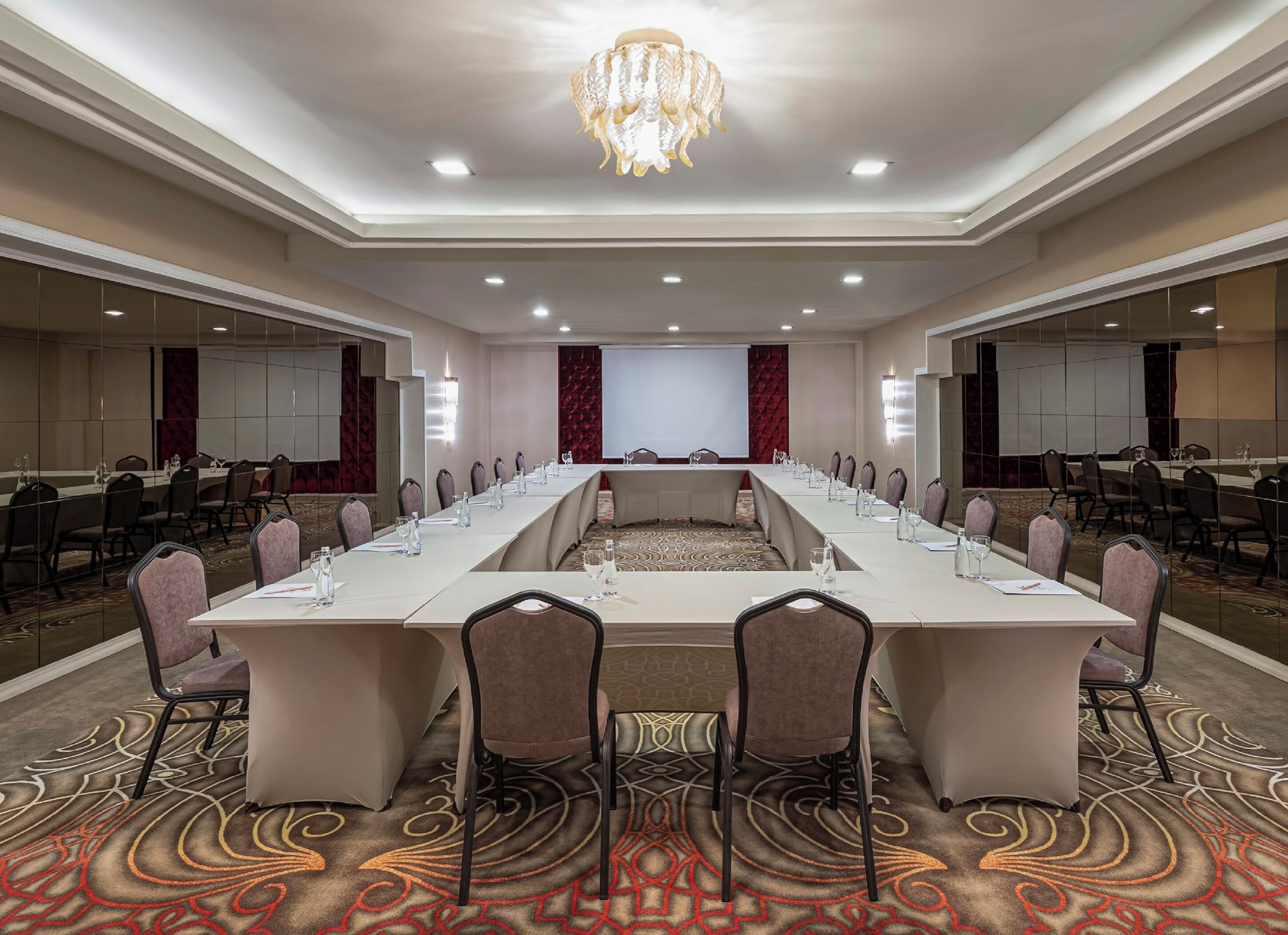 Un salón de conferencias con una larga mesa, sillas y una pantalla para proyector.