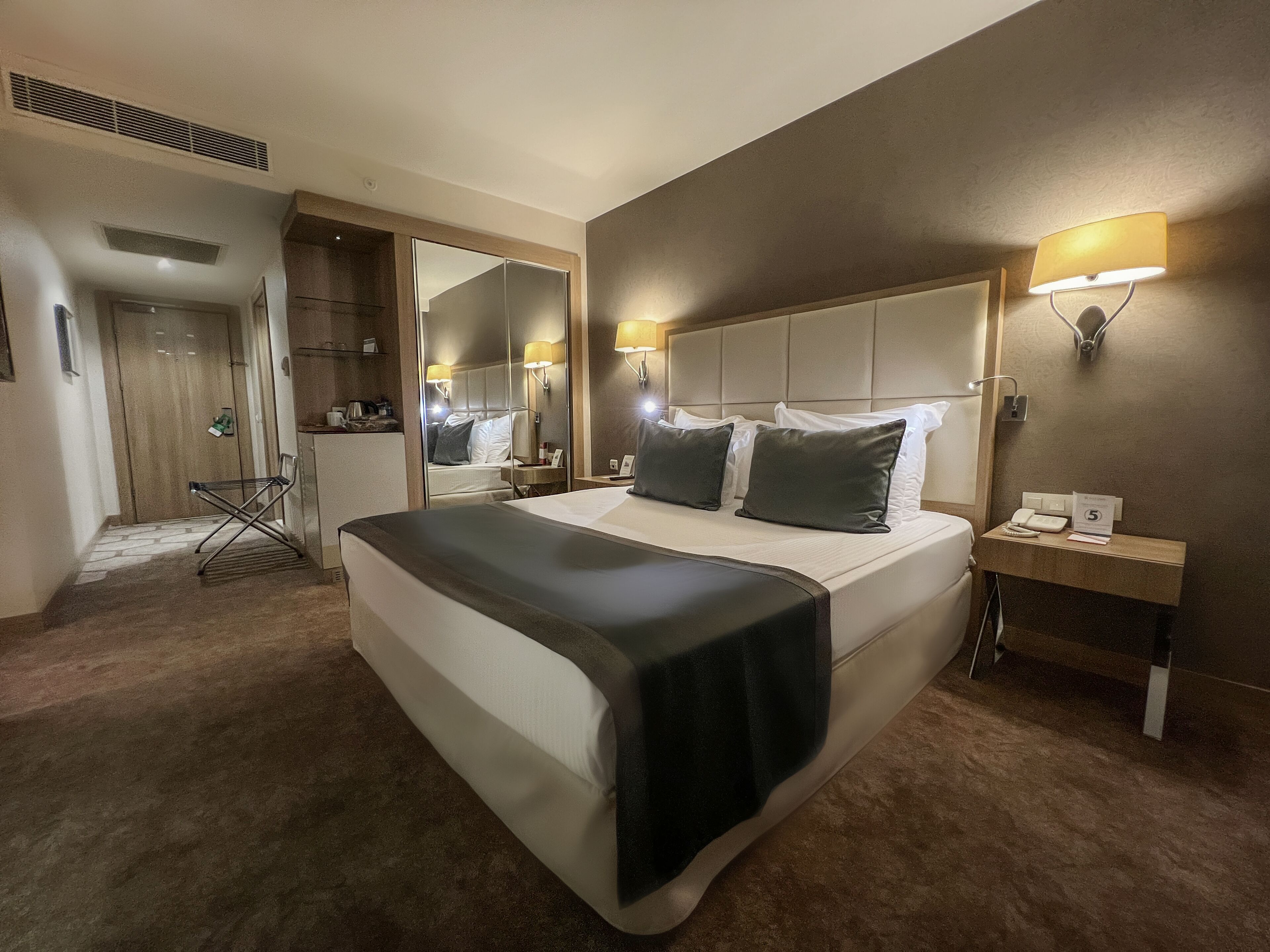 A hotel room with a large bed, bedside lamps, a nightstand with a phone, and a mirror.